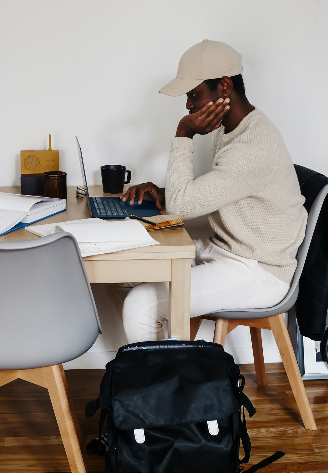 Un enseignant à sa table de travail, la main sur le visage, devant un cahier ouvert et une pile de copies.